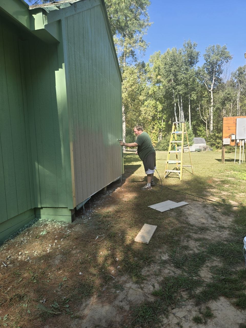 Jeff spraying the storage building exterior with the wrong paint color during the September 2025 push