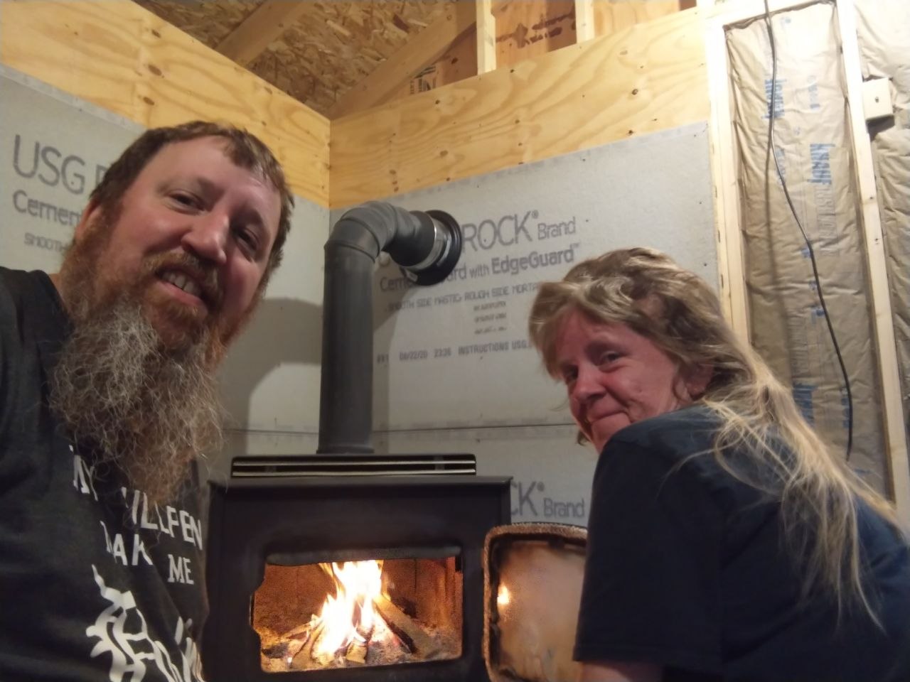 Jeff and Vanessa sitting by the stove in the early unfinished cabin